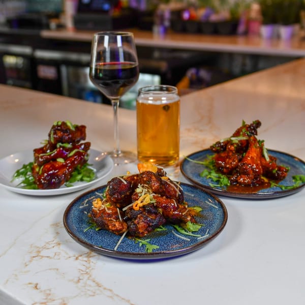 Three plates of Caribbean-style chicken wings with drinks on a marble bar top.