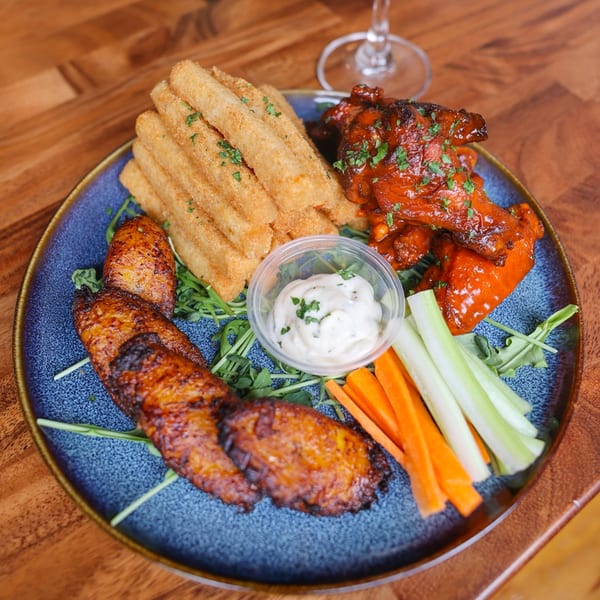 A blue plate with Caribbean food including chicken wings, fried plantains, breaded sticks, and vegetables.