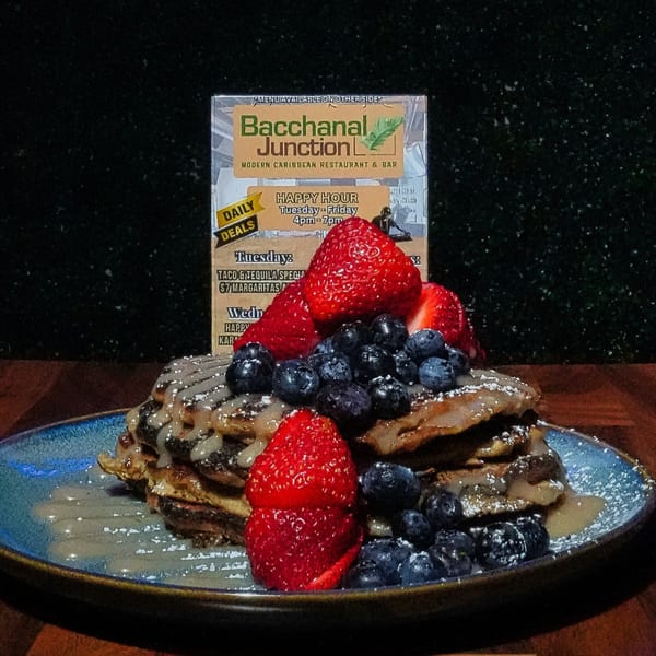 A stack of Bacchanal Junction's Caribbean pancakes topped with blueberries, strawberries, and syrup.