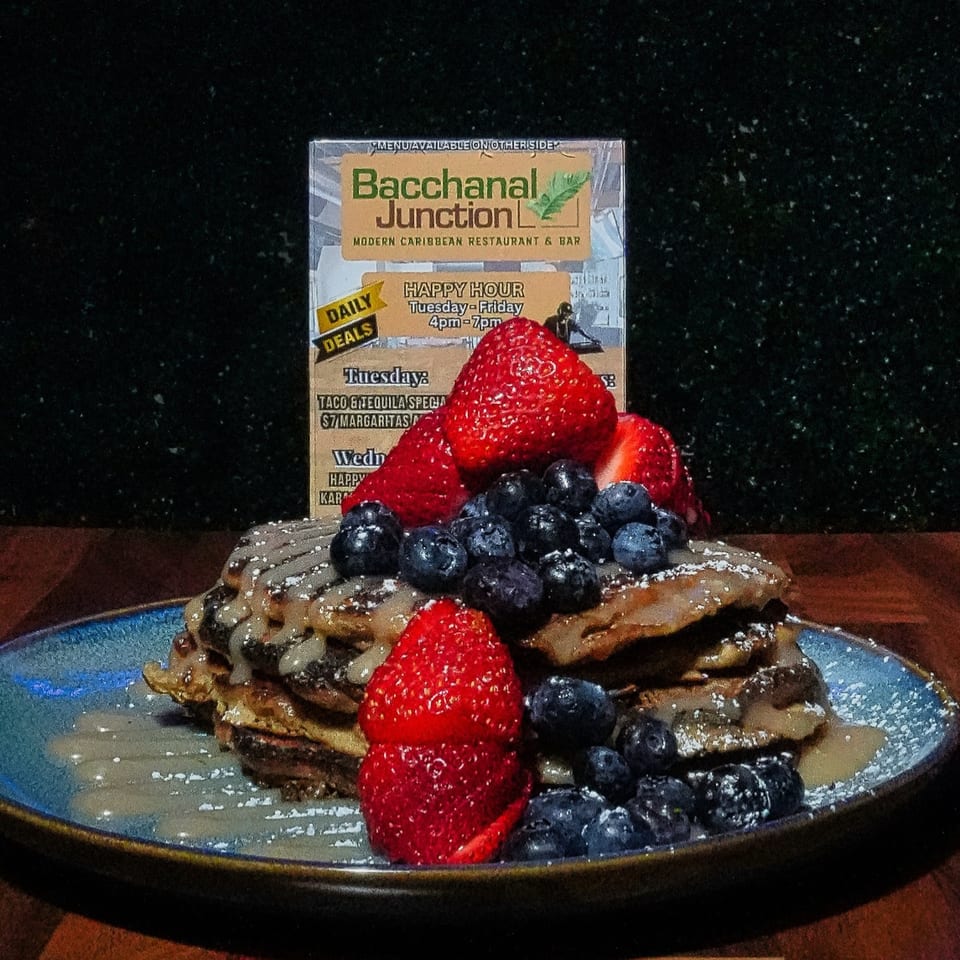 A stack of Bacchanal Junction's Caribbean pancakes topped with blueberries, strawberries, and syrup.